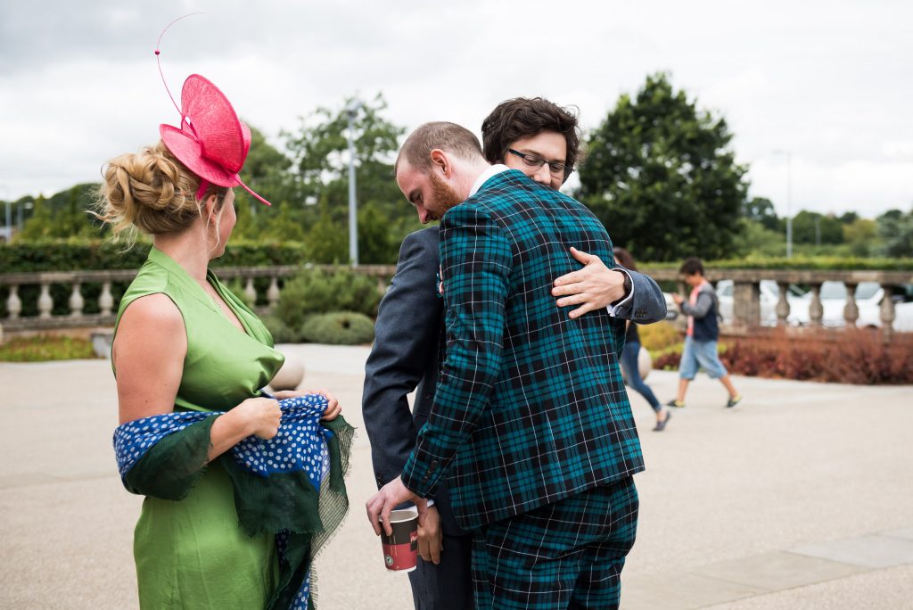 Quirky Groom wearing tartan suit hugs wedding guest Berkshire theatre wedding