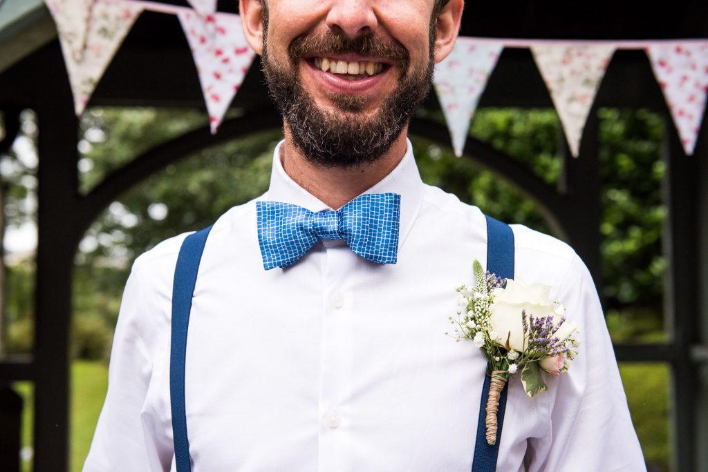 Groom wearing blue bow tie with bunting to decorate beach wedding Cornwall