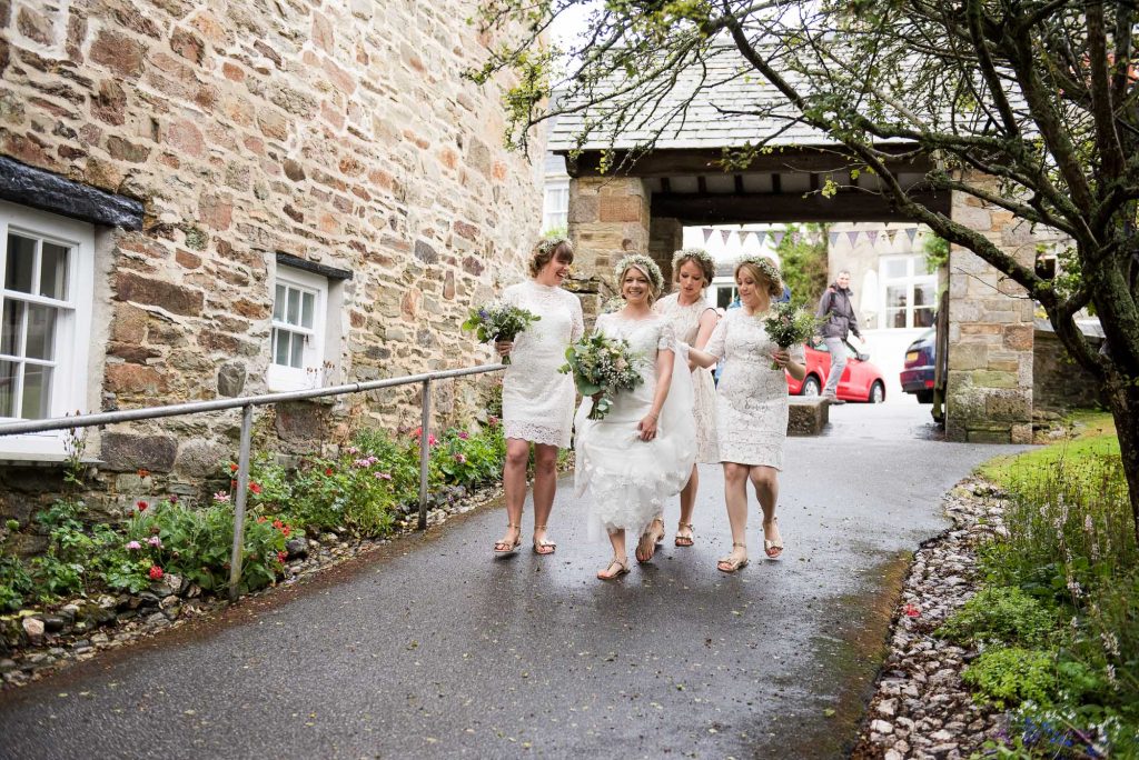 Bride with bridesmaids wearing lace white dresses walk together Cornwall
