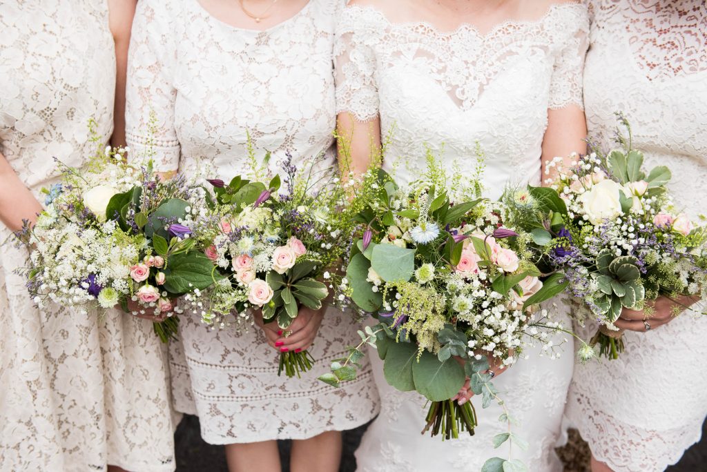Bride with bridesmaids wearing lace dresses holding rustic green floral bouquets