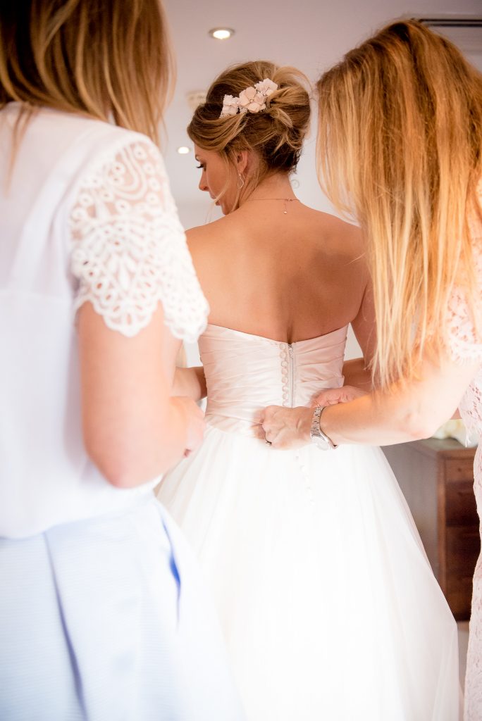 Great Fosters. Natural Wedding Photography. The Bride is Helped into her Ellis Bridal Wedding Dress.