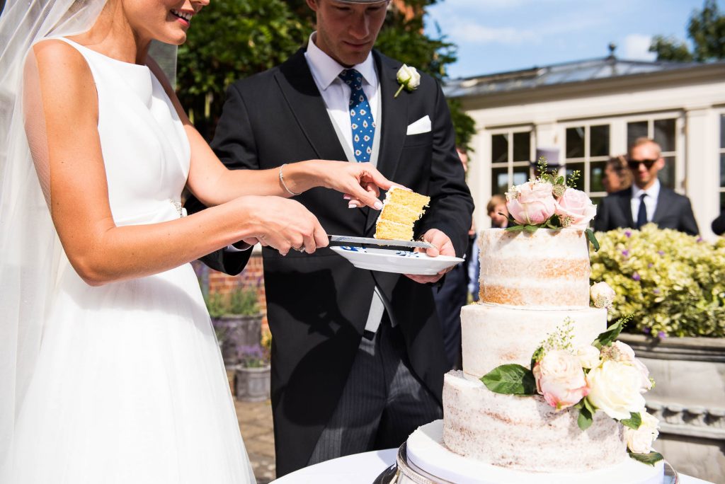 Outdoor Wedding Photography Surrey, Bride and Groom Cut Their Wedding Cake In The Sunshine Outside, Surrey Wedding Photography