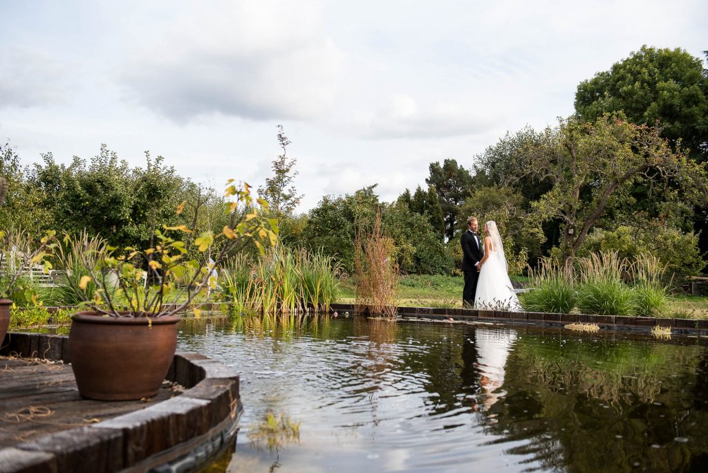 Outdoor Wedding Photography Surrey, Bride and Groom Stand by The Natural Pool