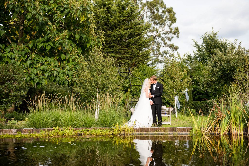 Outdoor Wedding Photography Surrey, Elegant Couple Embrace Each Other As Their Reflection Is Seen In The Lake