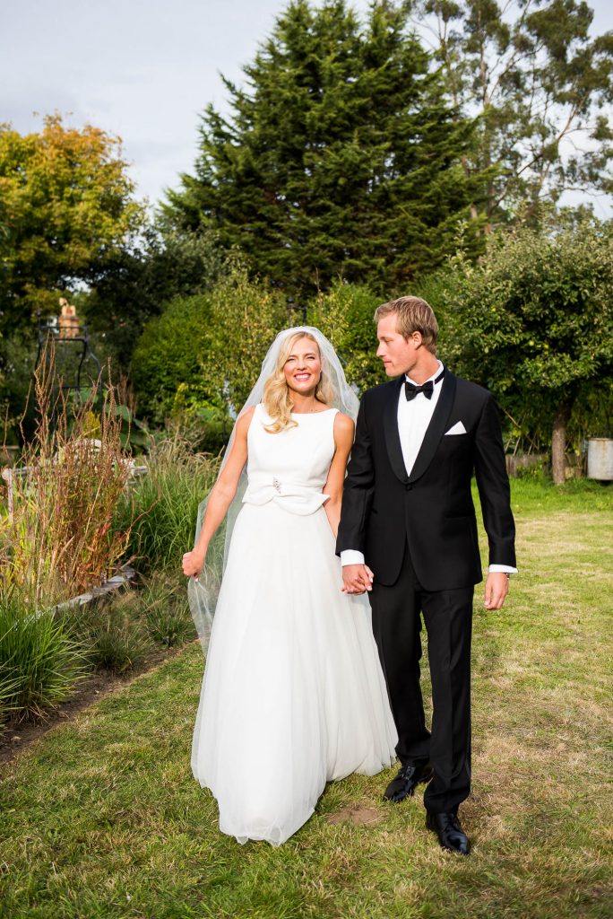 Outdoor Wedding Photography Surrey, Stylish Couple Walking Naturally Hand In Hand at Their Elegant Garden Wedding