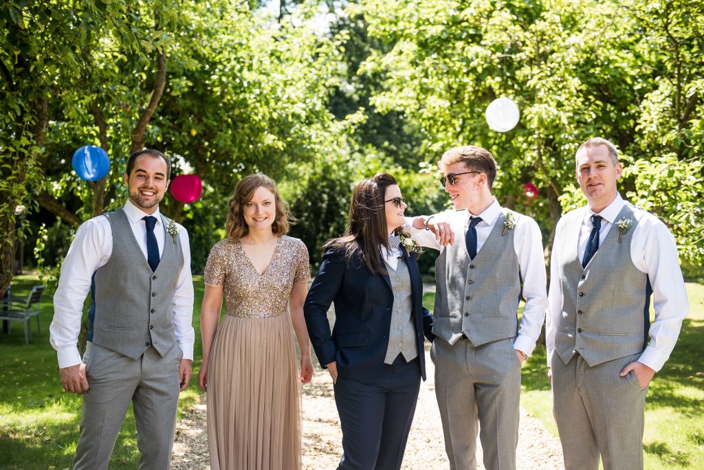 lgbt wedding photographer, Bride stands with her bridal party in a smart tailored suit and bow tie