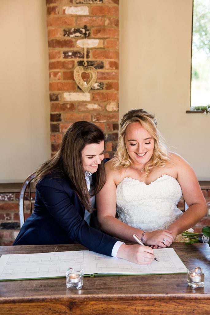 lgbt wedding photographer, brides sign the wedding certificate at gorgeous same sex ceremony at Dodmoor House