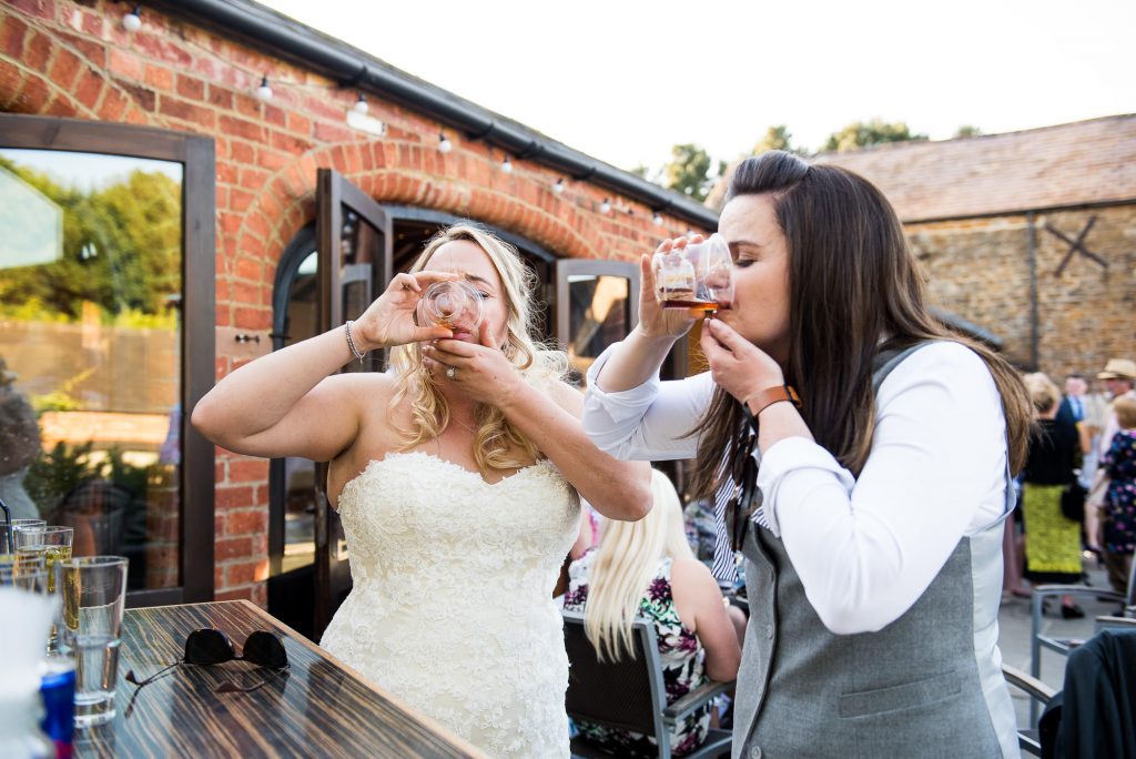 lgbt wedding photographer, two brides do shots together at the wedding bar