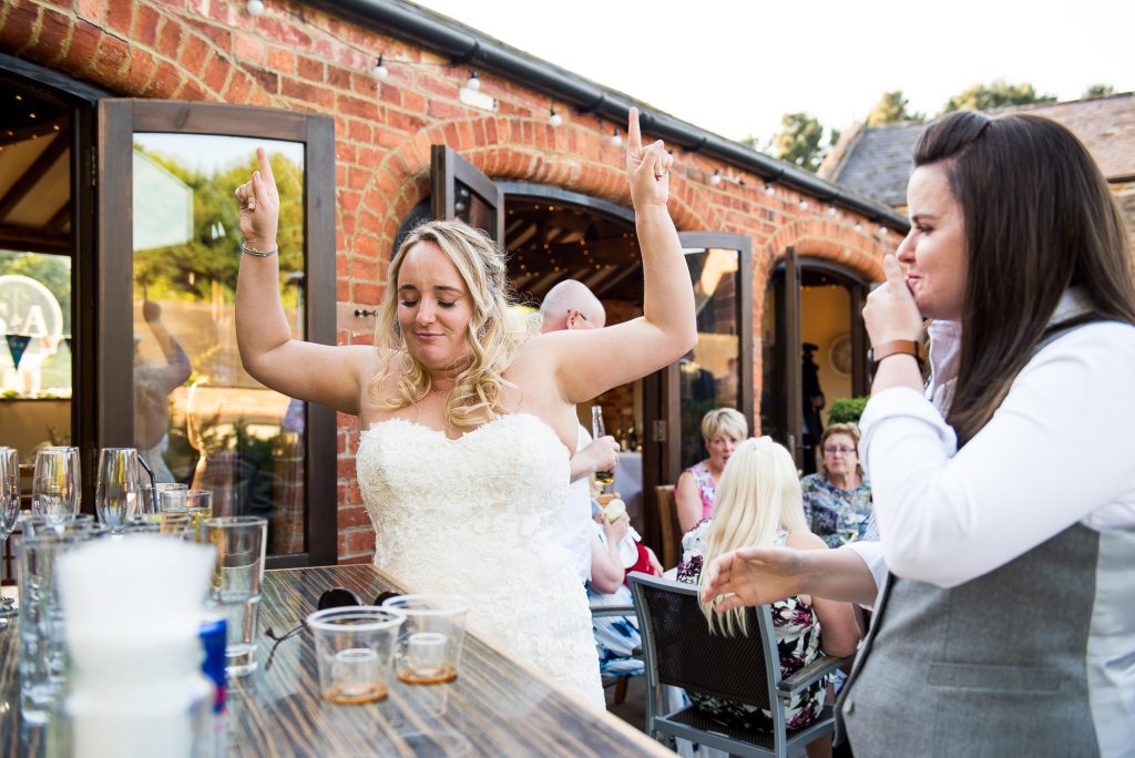 lgbt wedding photographer, two brides do shots together at the wedding bar