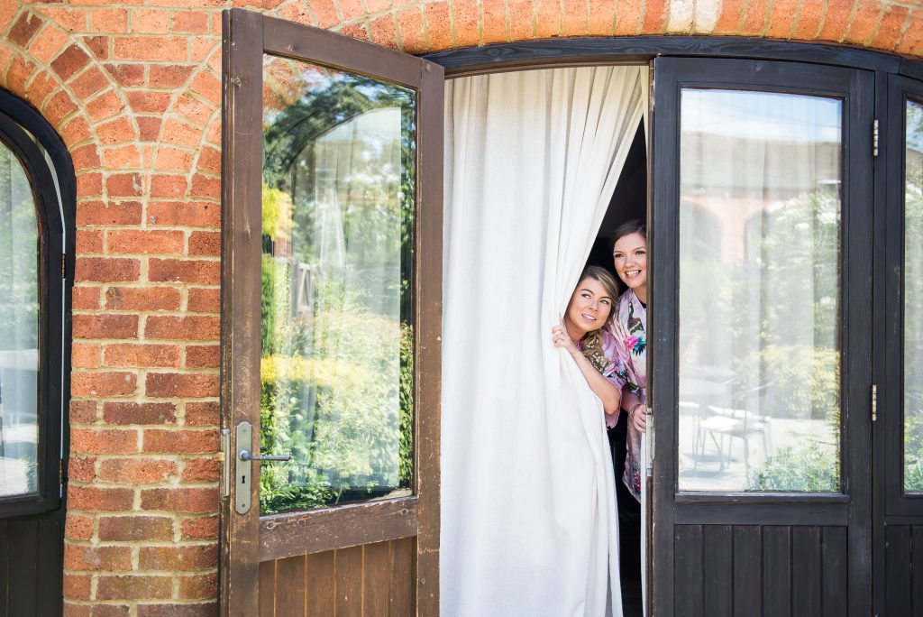 lgbt wedding photographer, Bridesmaids peering through curtains at Dodmoor House