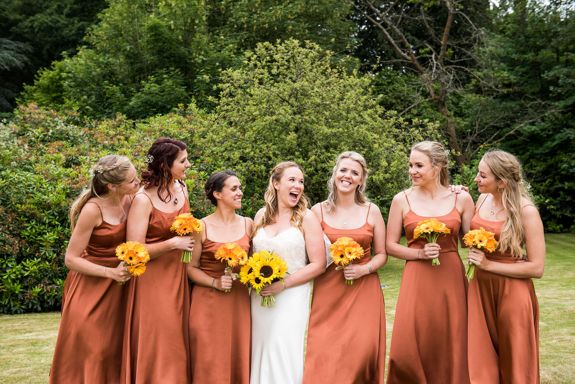 creative wedding photography surrey, bride laughs with her bridesmaids dressed in matching burnt orange strappy dresses