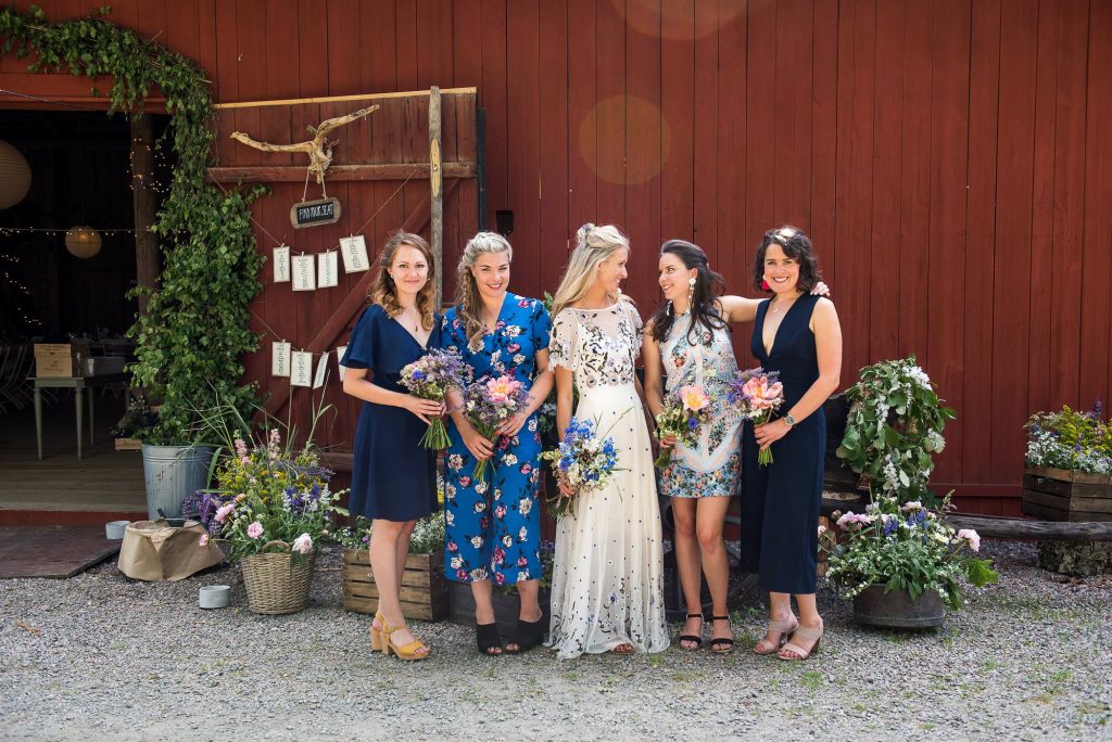 bride stand with bridesmaids in front of gorgeous traditional Swedish red barn