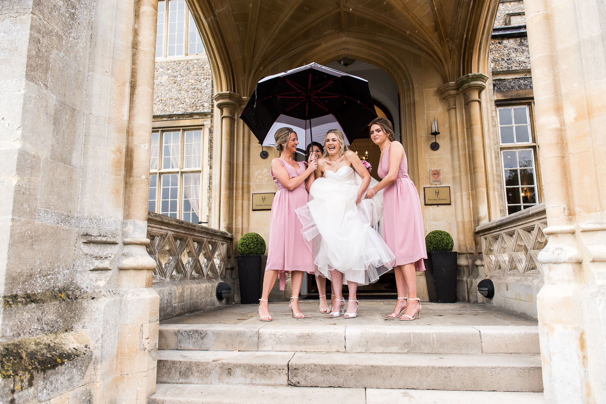 Fun wedding photography, gorgeous laughing bride being helped to the car in the rain by her bridesmaids