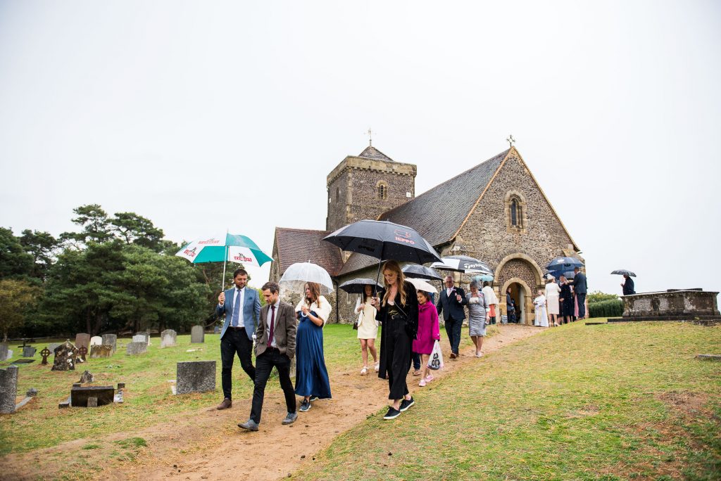 Fun wedding photography, guests walk with umbrellas from a wedding ceremony 