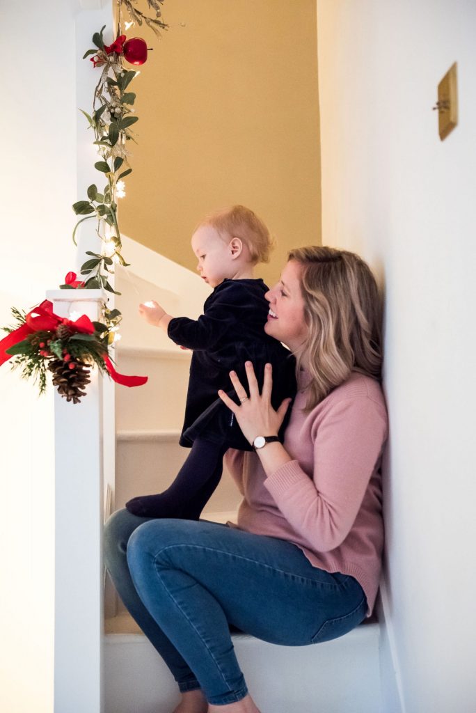 Mother and daughter sit on the stairs adorned with Christmas decorations