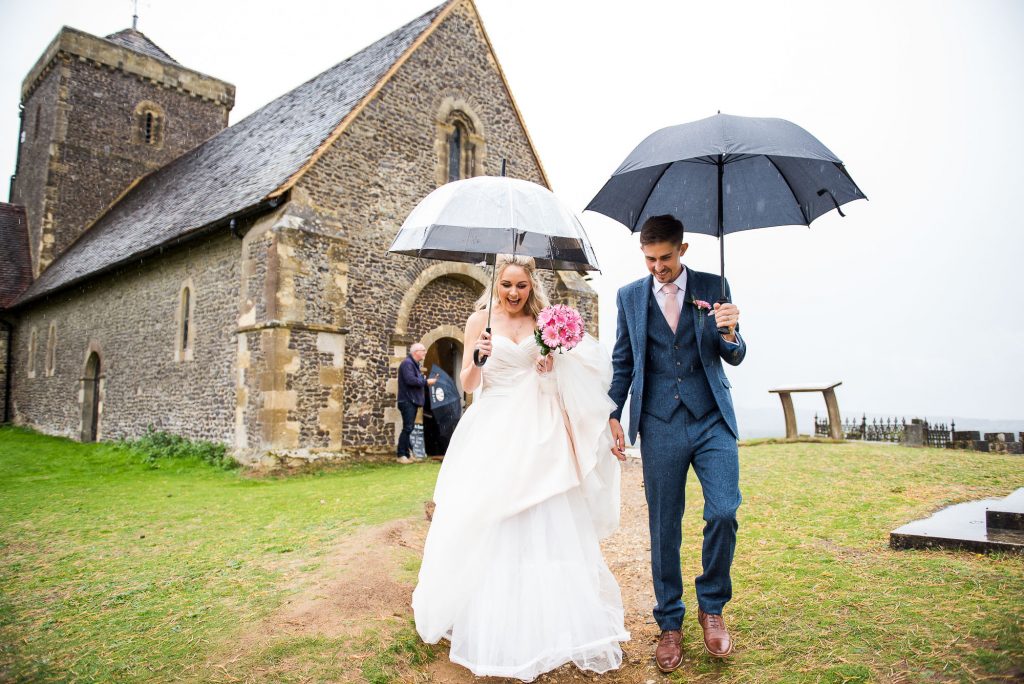 st martha's wedding, couple walk down under umbrellas from the church 