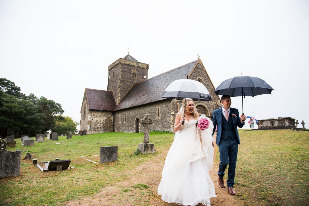 st martha's wedding, couple walk down under umbrellas from the church