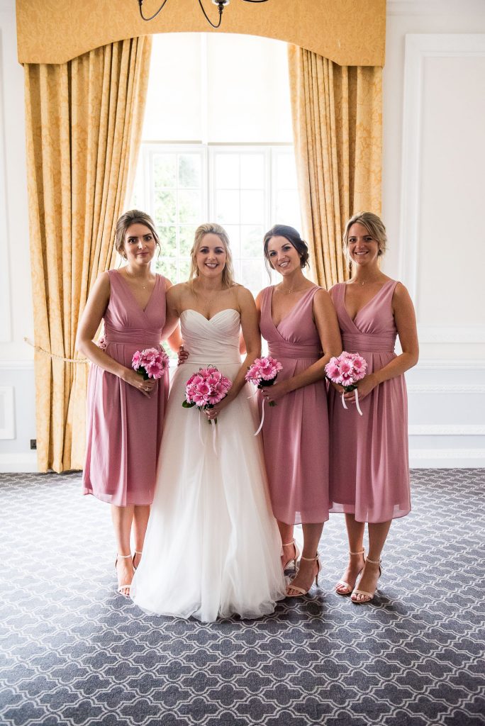 bride with her bridesmaids, dressed in matching soft pink midi dresses