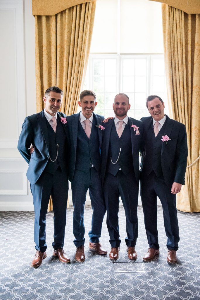groomsmen in matching three piece suits and pink handkerchiefs 