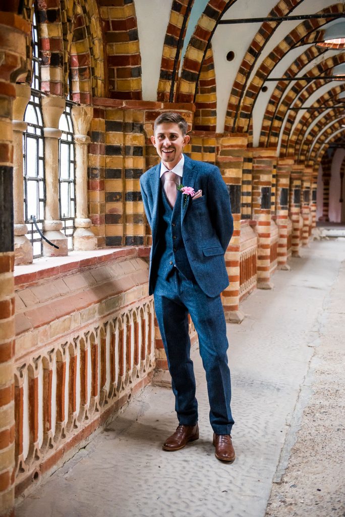 groom in a textured three piece blue suit with pink handkerchief and matching button hole 