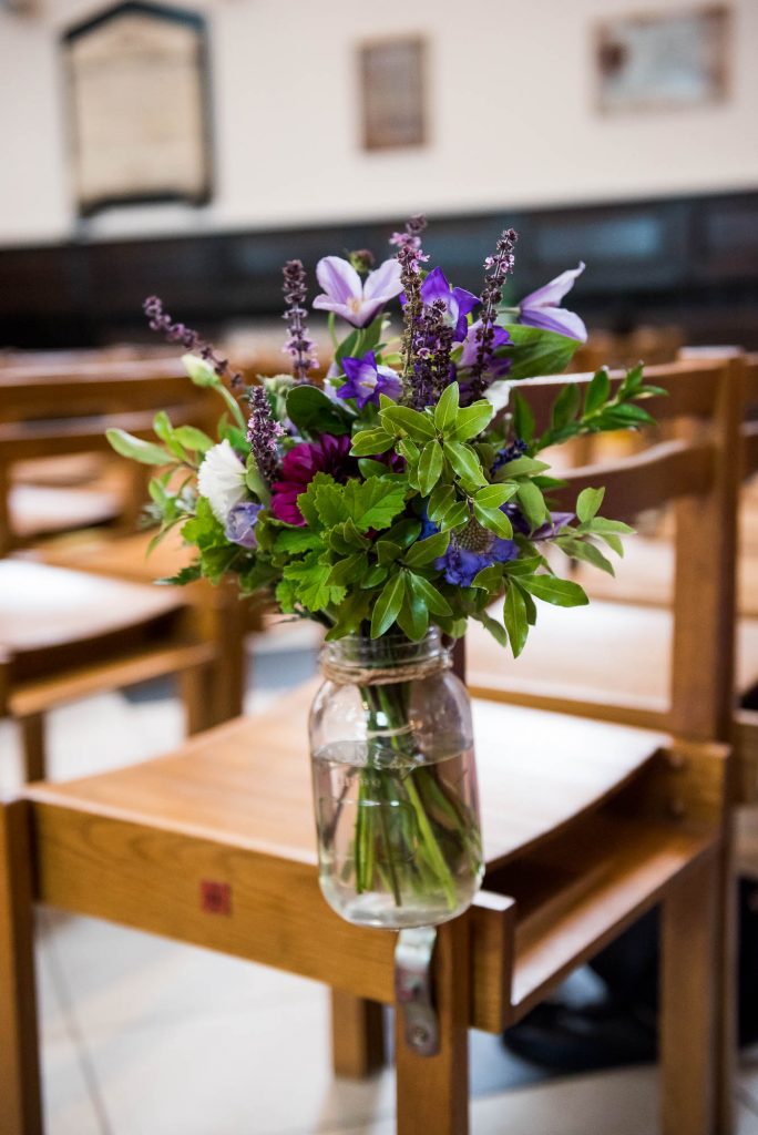 Purple, green and white ceremony flowers in rustic glass jars with twine