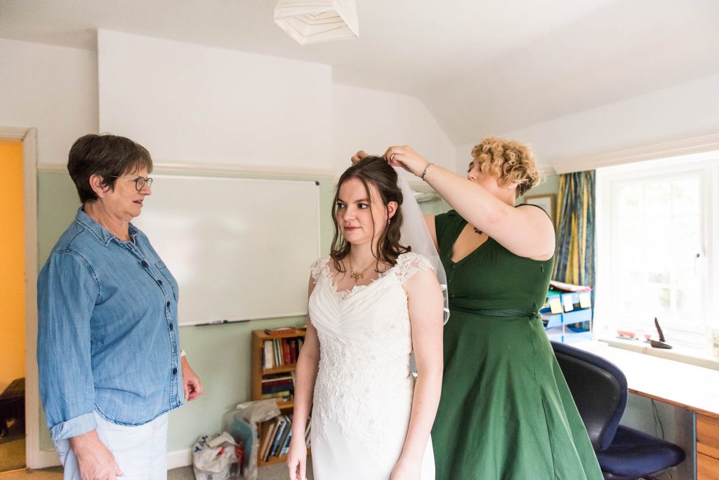 Bride in white lace dress is helped by her bridesmaid whilst putting on her veil