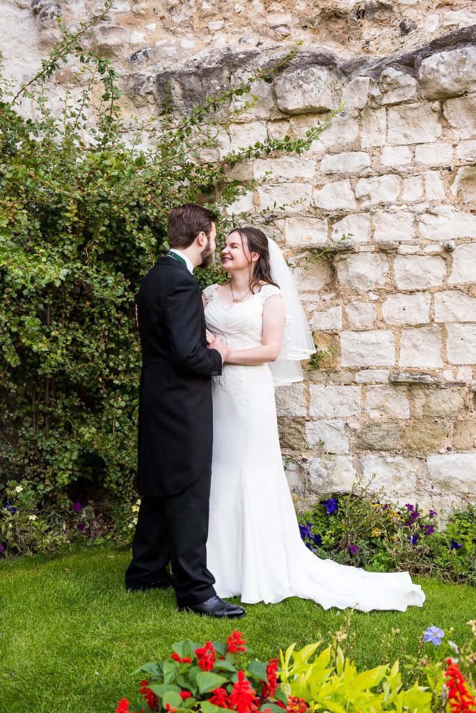 Couple stand looking at each other in front of a white stone wall covered in ivy