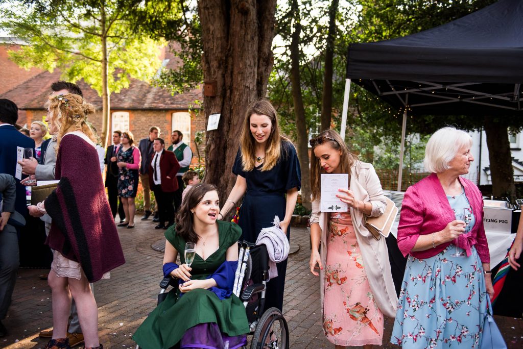 Bridesmaid in a wheel chair is pushed by guests at the reception, Documentary wedding photographer surrey