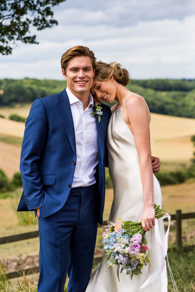 Surrey wedding couple laugh together. Bride wears a backless silk wedding dress and the groom is in a navy blue suit