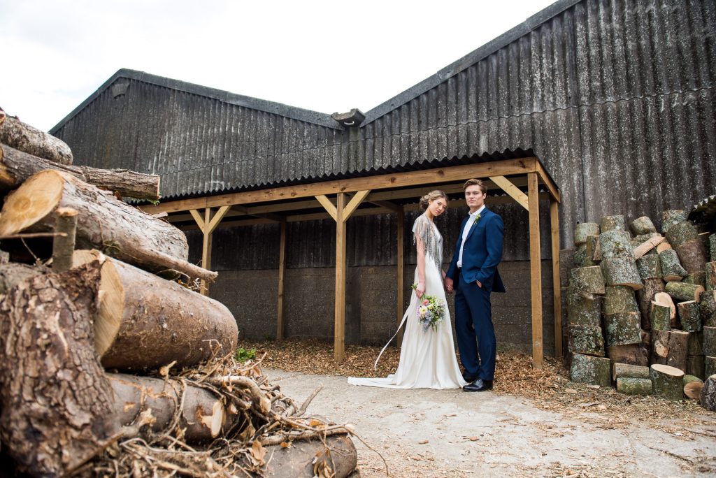 Couple stand in a rustic barn setting holding hands
