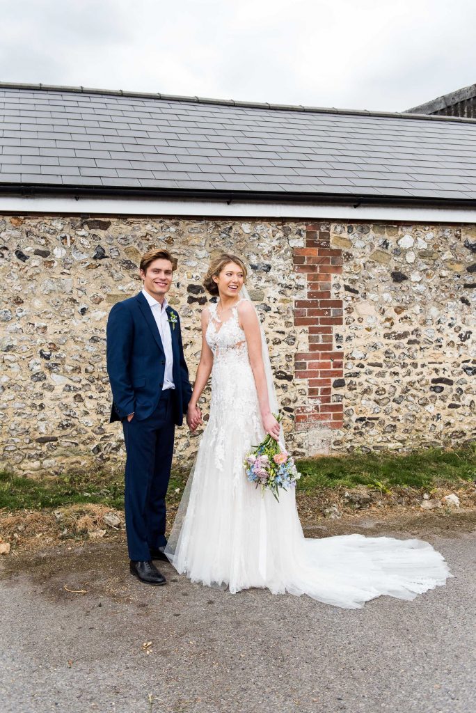 Gorgeous couple stand hand in hand in front of stone barn