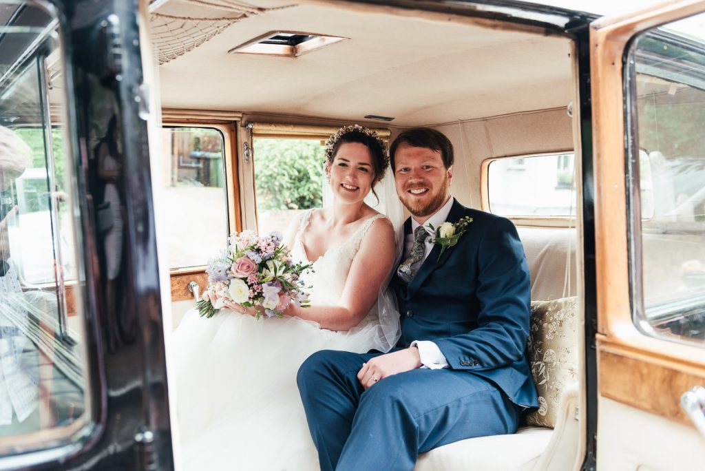 Bride and groom smile inside their vintage wedding car