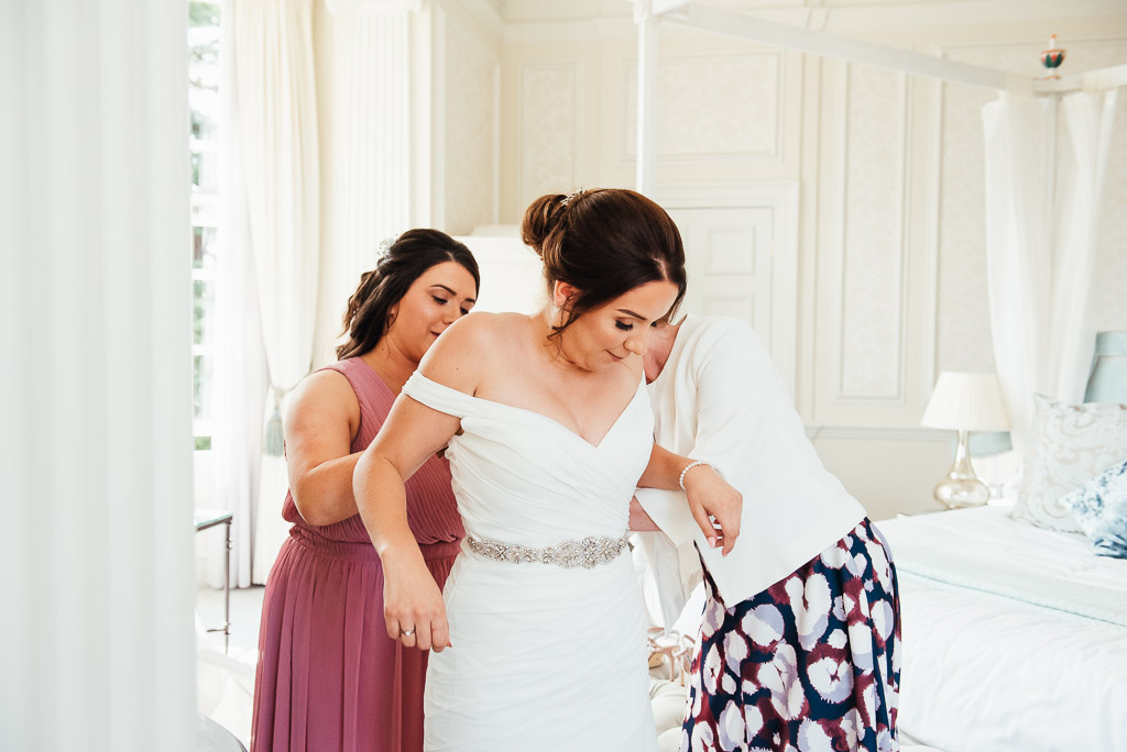 Bride is helped into her wedding dress by her maid of honour 