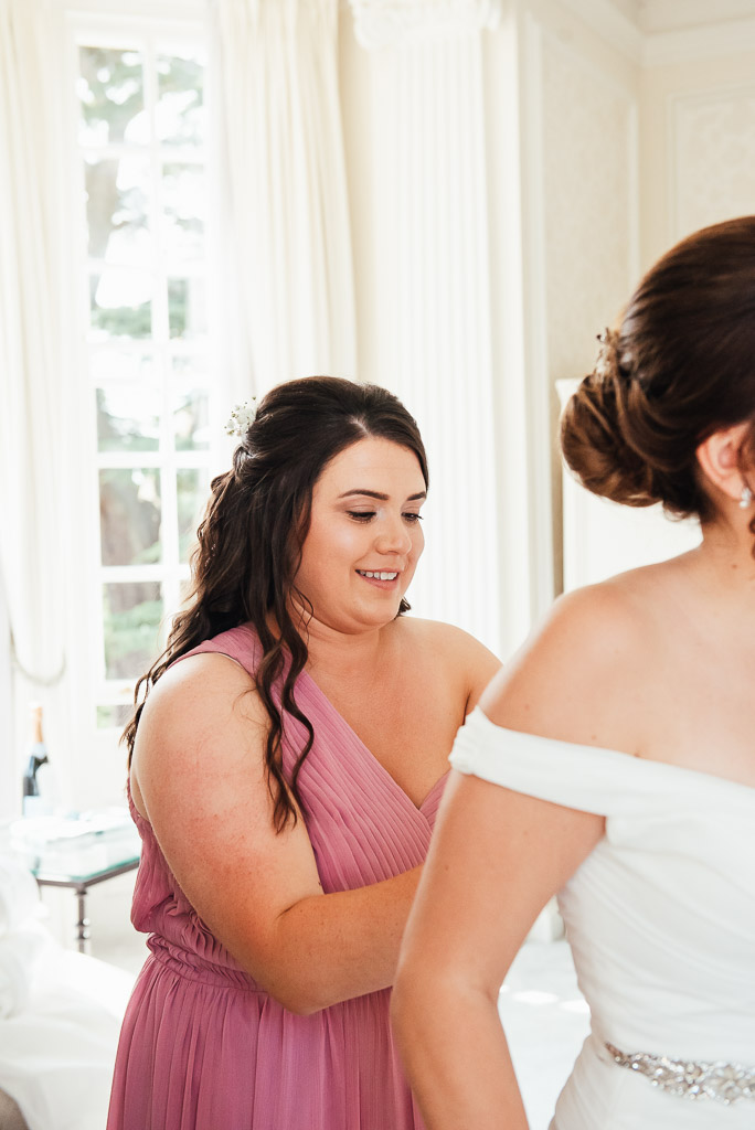 Bride is helped into her wedding dress by her maid of honour 