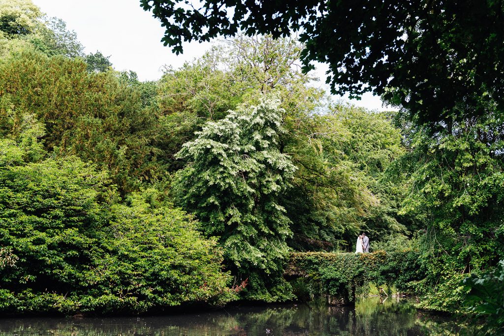Couple stand embracing on a bridge surrounded by green foliage