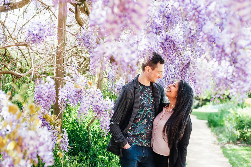 Couple stand together with wisteria all around them for creative engagement photography