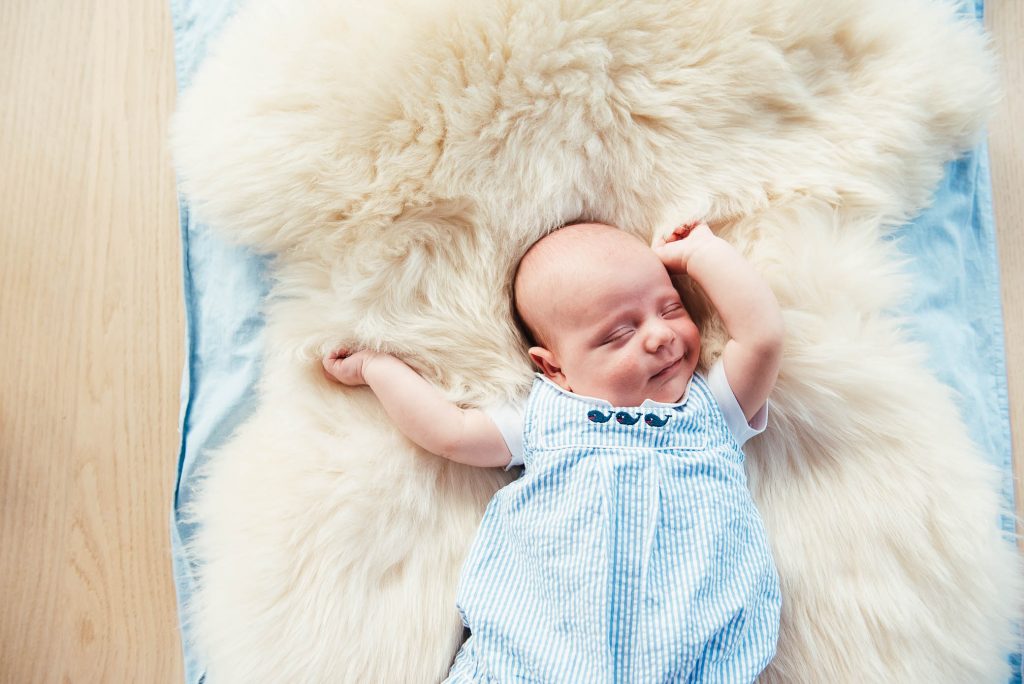 Newborn baby sleeps on a sheepskin rug and stretches 