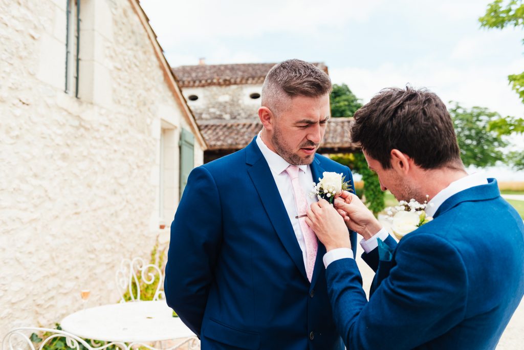 Groom helps best man with his button hole
