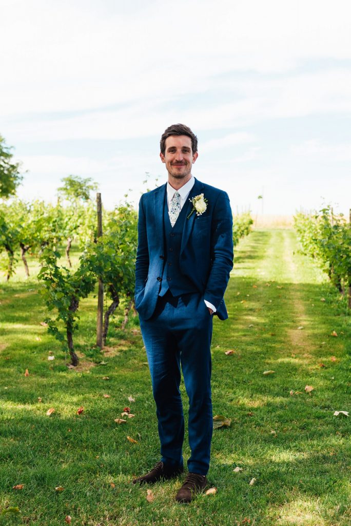 Handsome groom in a tailored navy blue three piece suit with home made button hole