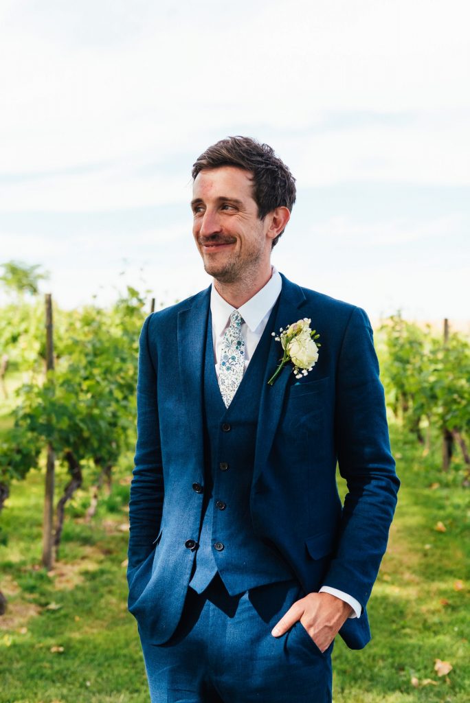 Handsome groom in a tailored navy blue three piece suit with home made button hole