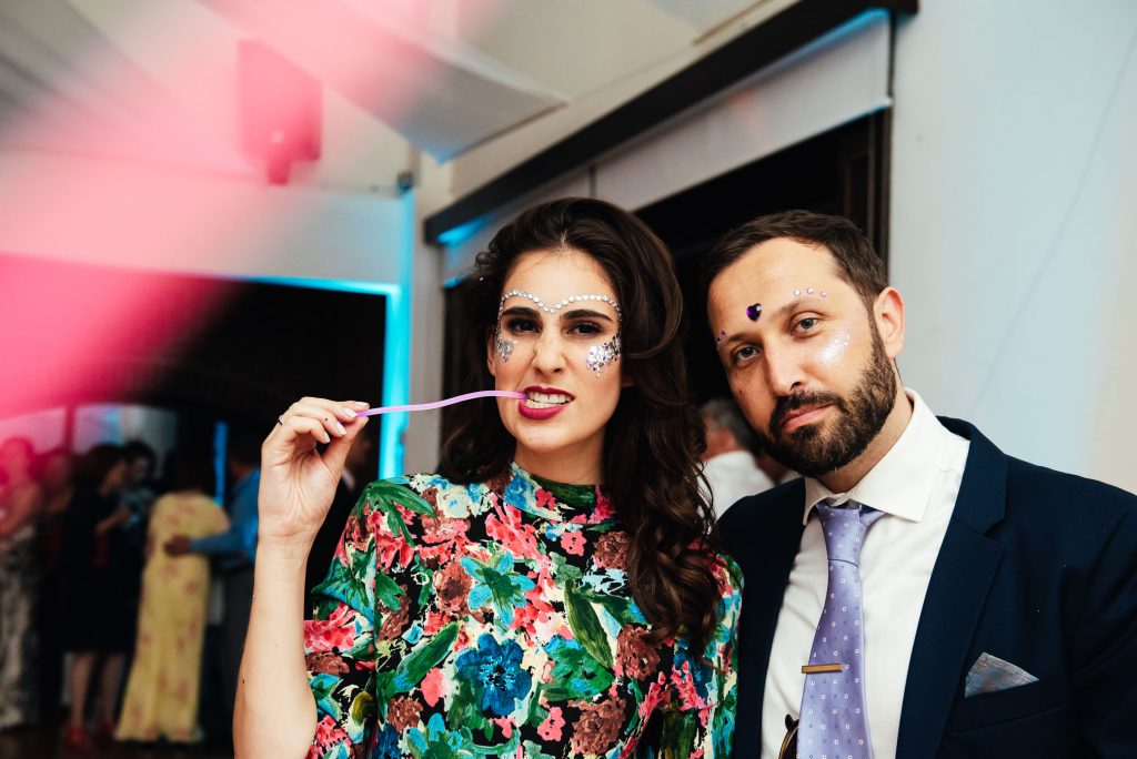 Quirky couple pose with face paints and glow sticks for a fun wedding photography