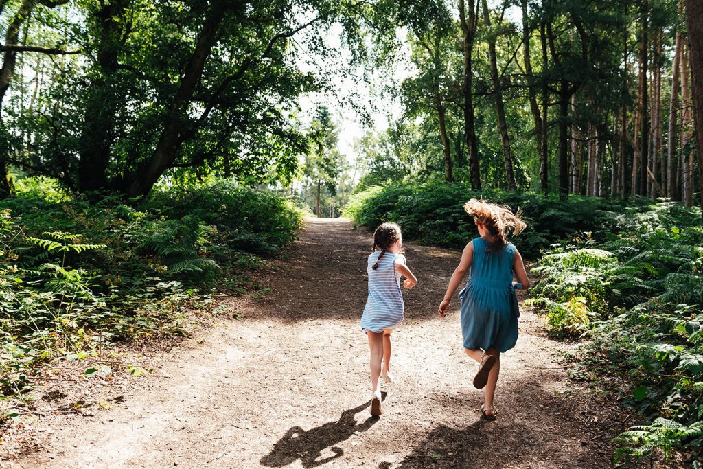 Children run freely in the woodland on an outdoor Surrey family photoshoot