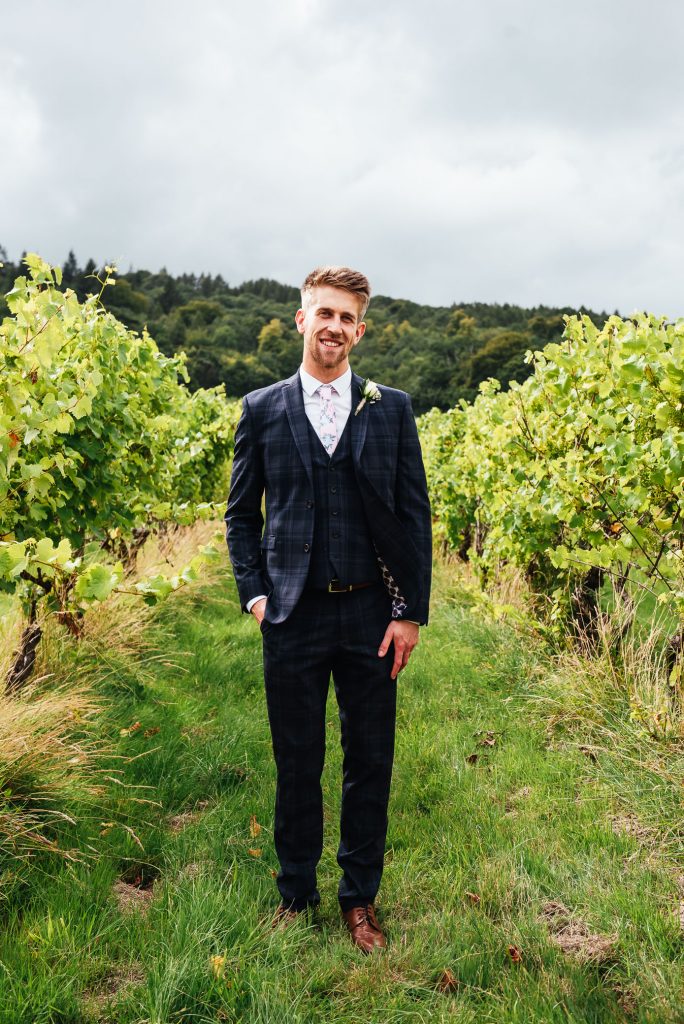 Handsome groom in a tailored navy blue three piece suit with chic white button hole