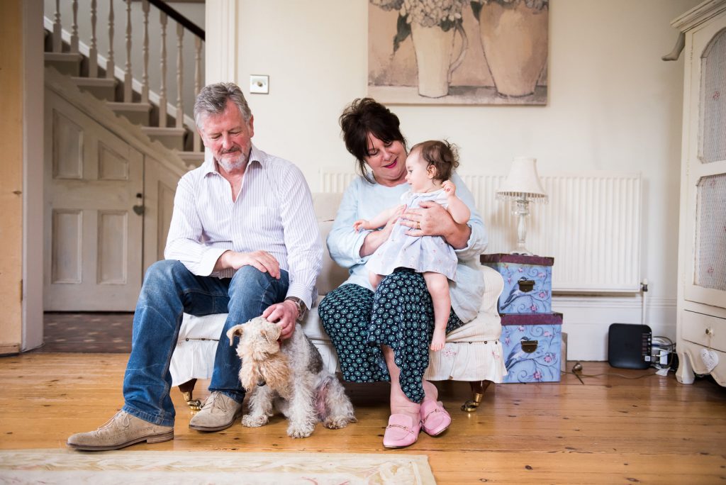 Grandparents sit together with granddaughter and dog at relaxed London family photography shoot at home