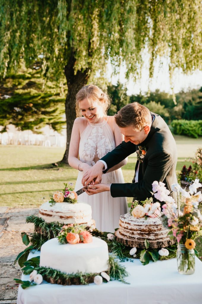 Couple Cut The Cake Outdoors - Summer Cain Manor Wedding