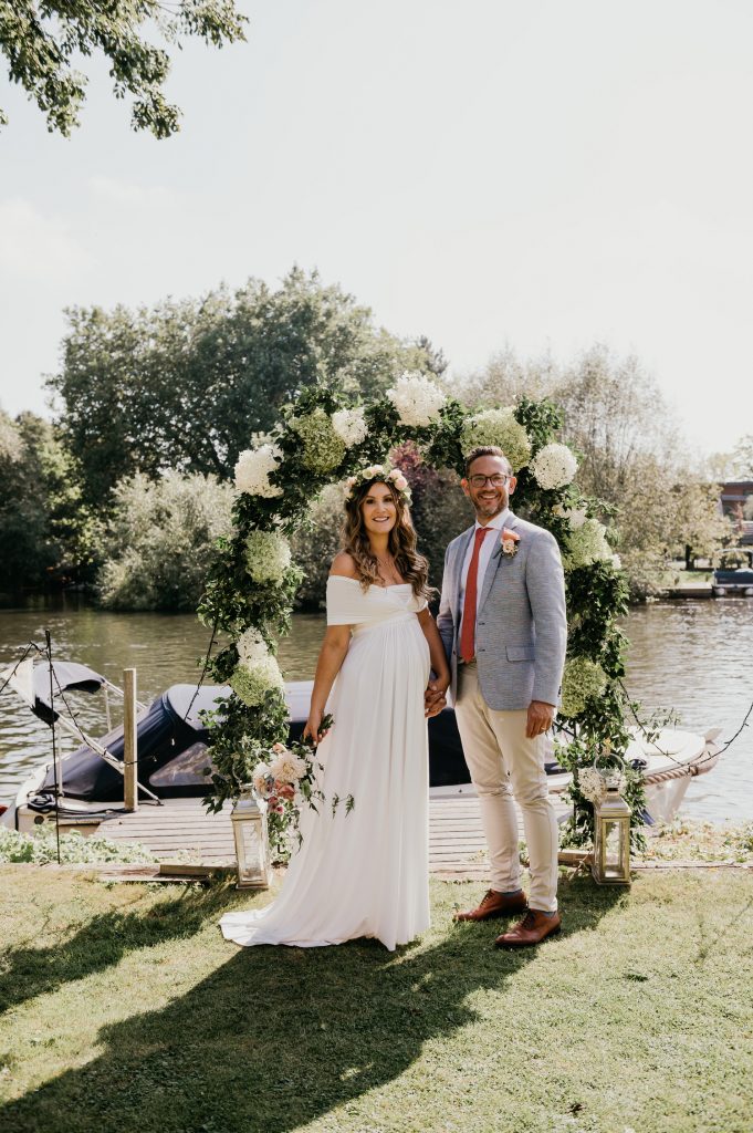 Couple Stand in Front of Floral Arch and River at Garden Marquee Wedding