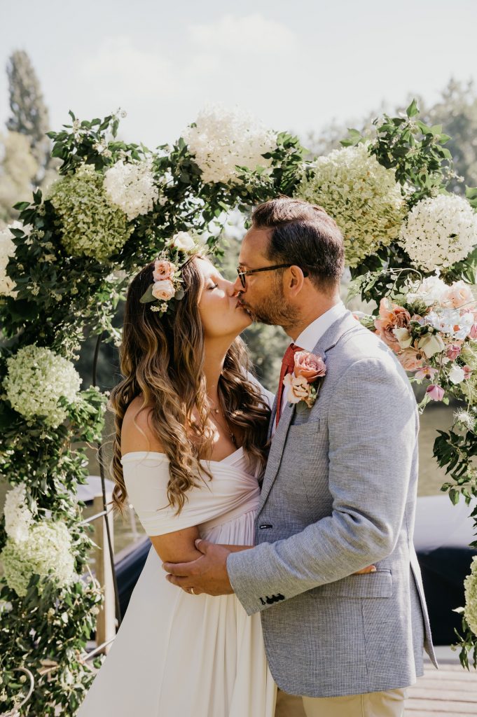 Couple Kiss in Front of Floral Arch and River at Garden Marquee Wedding