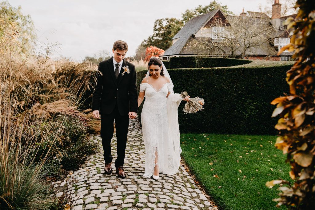 Couple walk hand in hand together through gardens at Bury Court Barn.