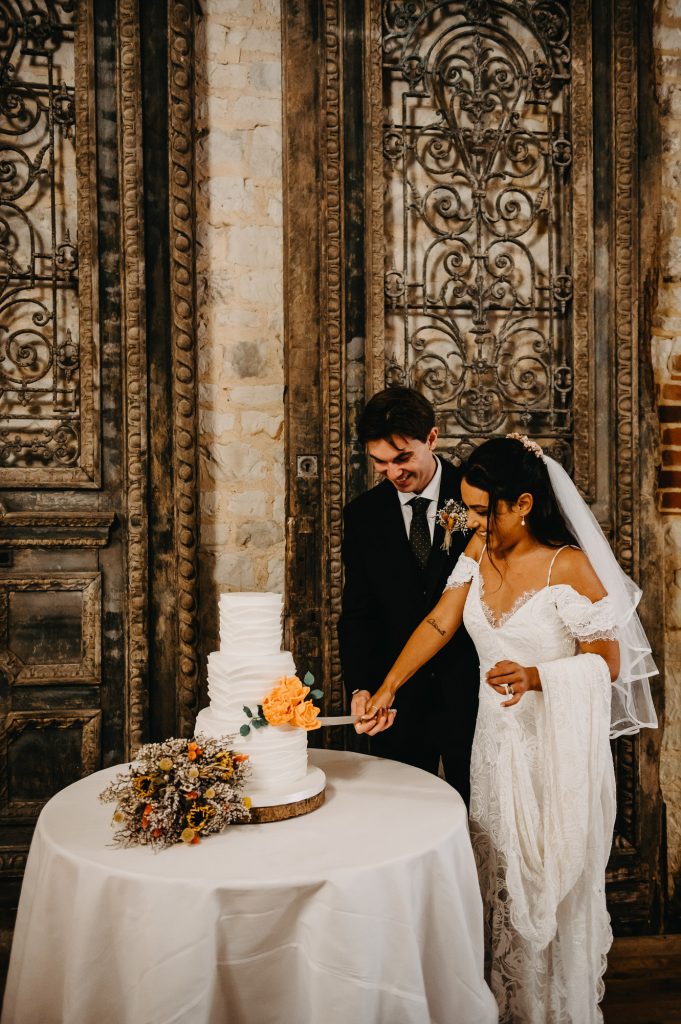 Relaxed and Natural Wedding Photography - Couple stand together and cut the wedding cake.
