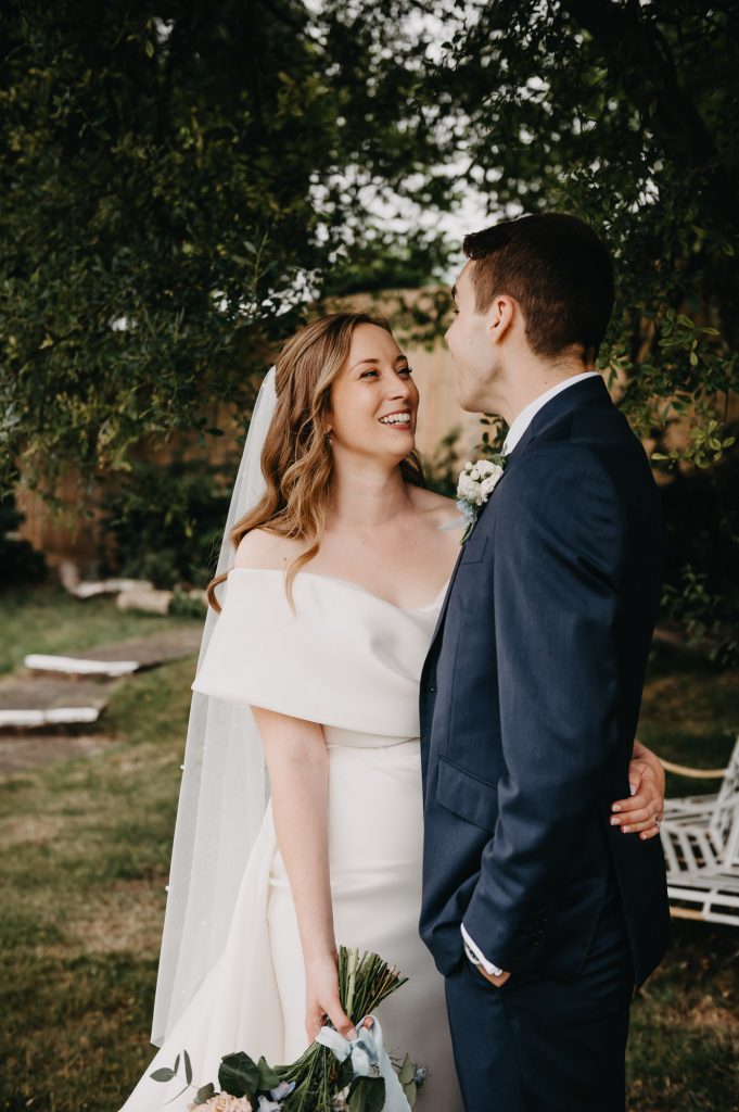 Relaxed and candid outdoor wedding portraits. Couple hug and laugh with one another in candid embrace.